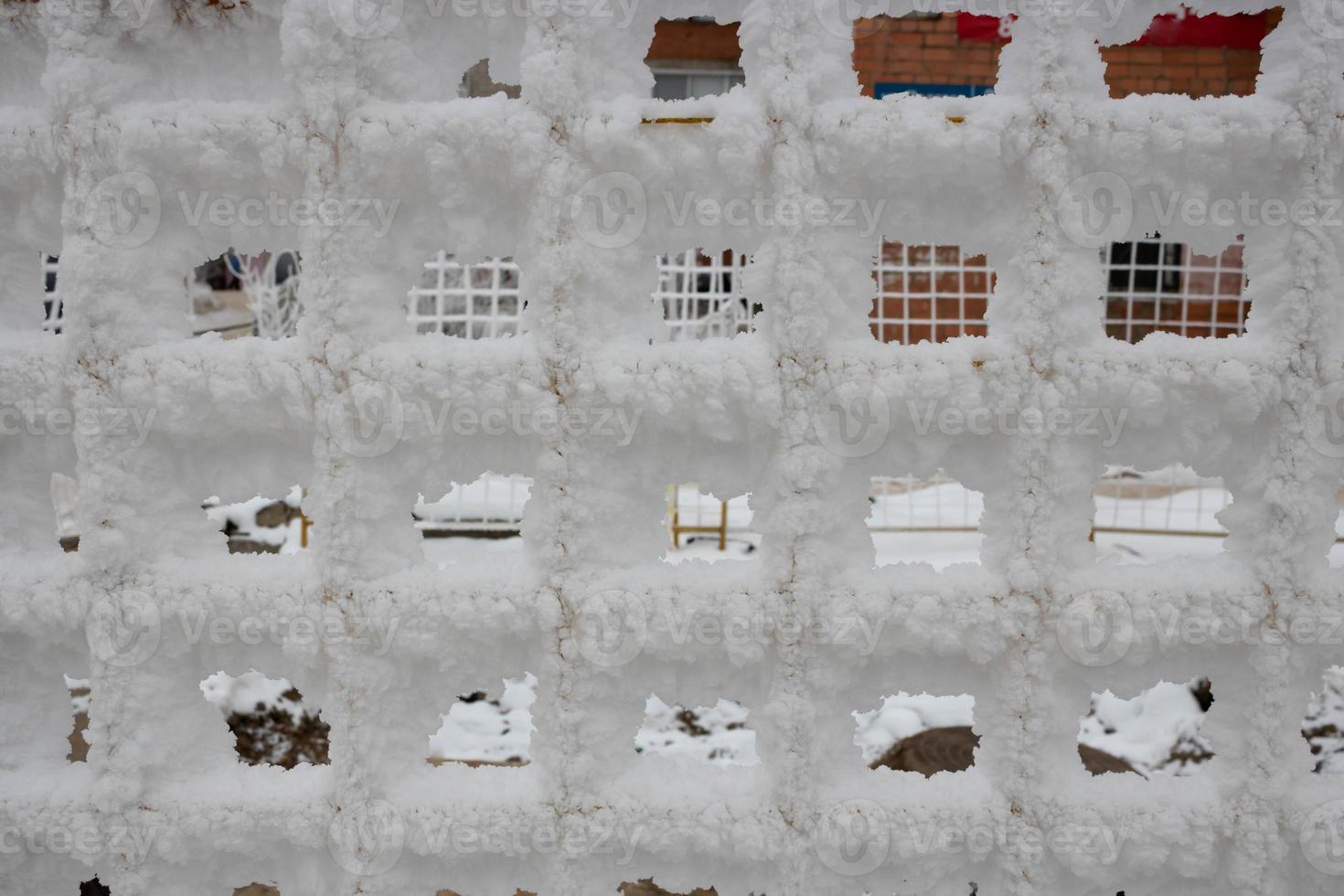 The fence grid is strewn with frost crystals, snowflakes. Winter snowy frosty background. World Snow Day photo