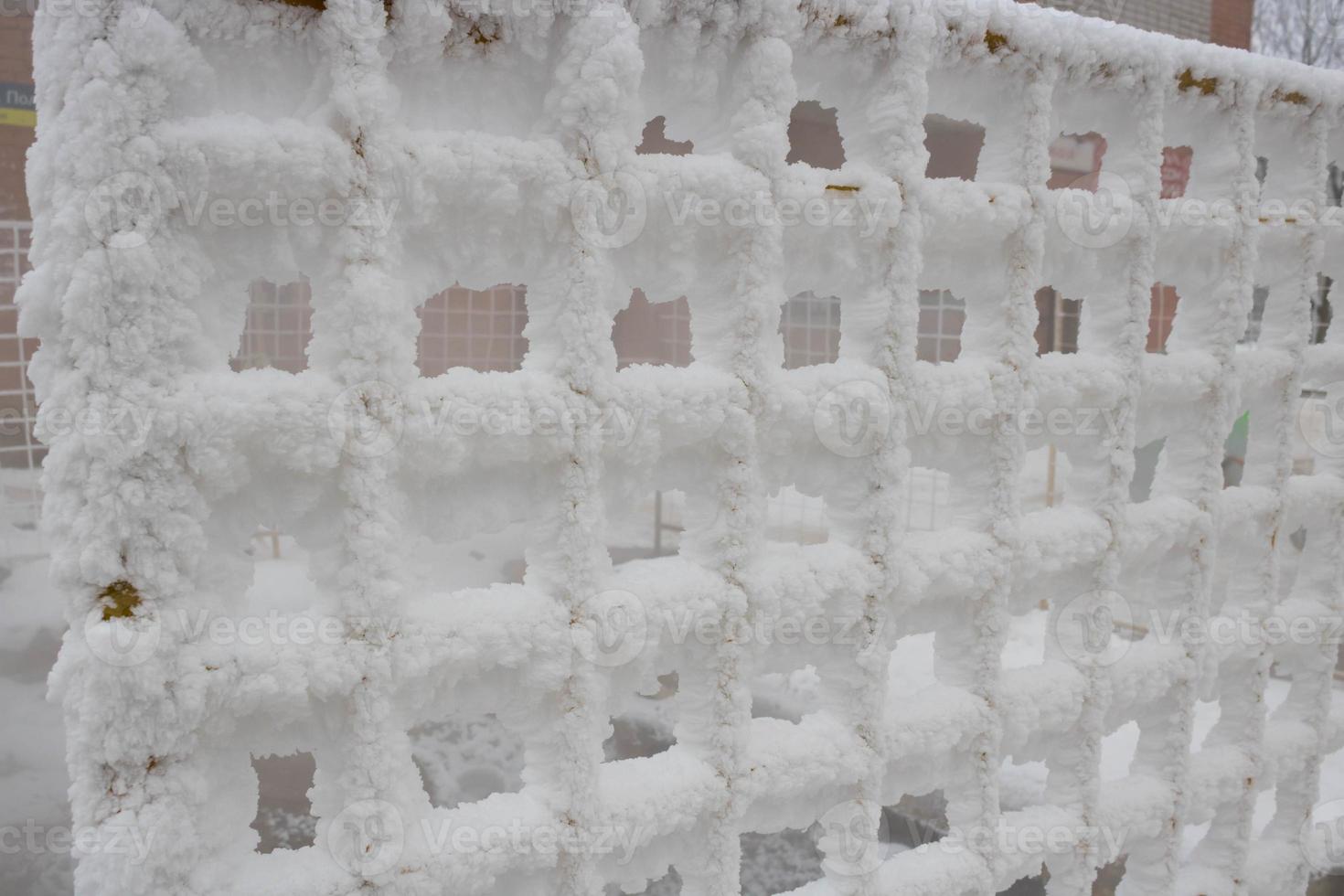 The fence grid is strewn with frost crystals, snowflakes. Winter snowy frosty background. World Snow Day photo
