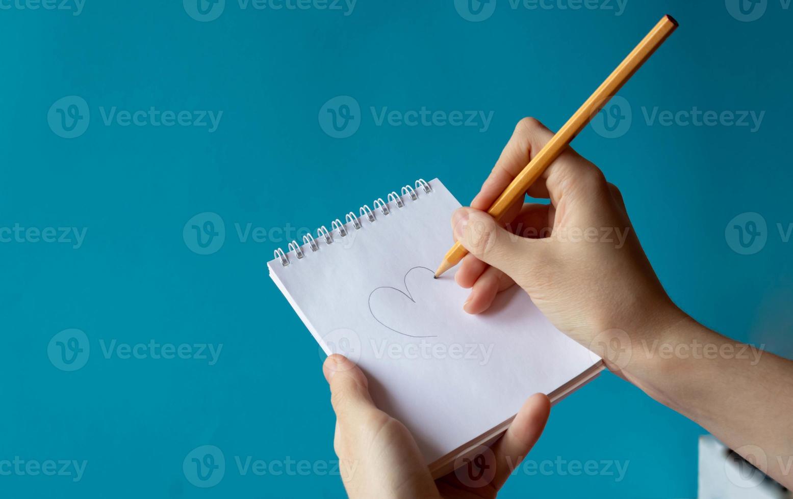 A hand with a pencil writes in a notebook on a blue background. Place for your text photo