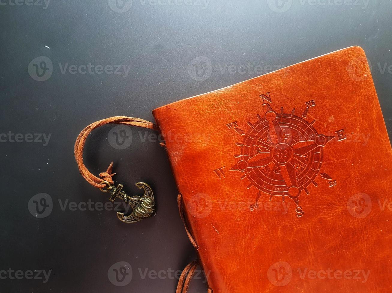 A notebook with a brown leather cover with a compass motif and anchor strap. photo