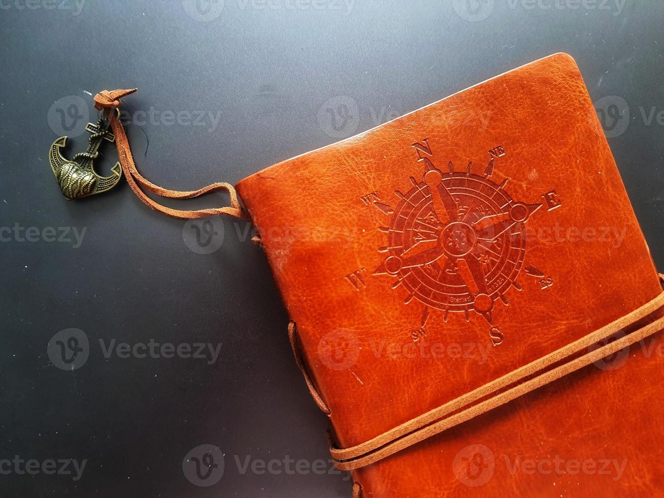 A notebook with a brown leather cover with a compass motif and anchor strap. photo