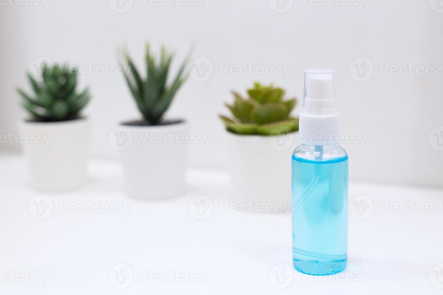 spray de alcohol puesto sobre la mesa blanca que tiene cactus verdes como fondo. foto