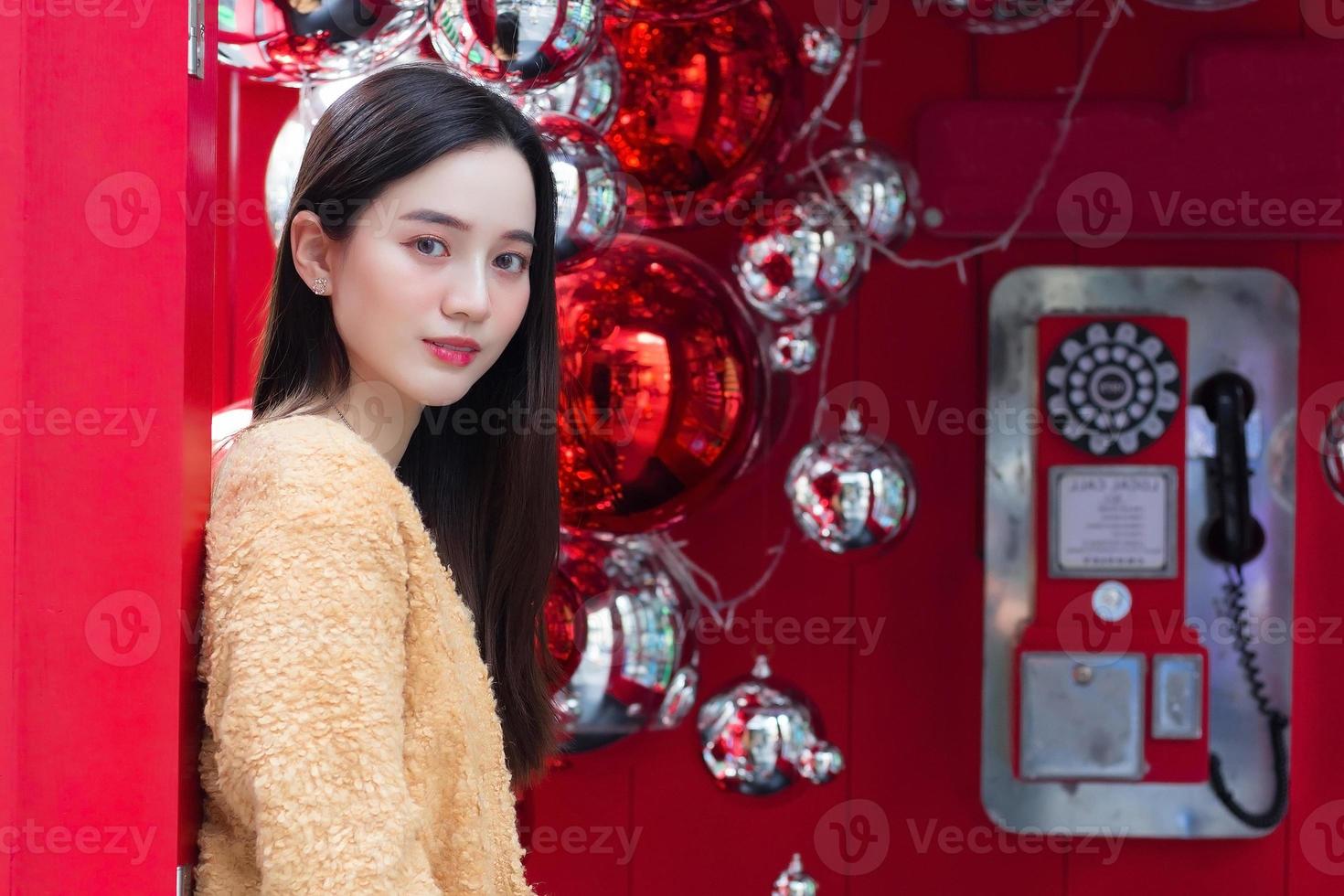 Asian beautiful woman long haired  wearing a yellow robe  and smiling happily standing in front of a red telephone booth In the theme of celebrating Christmas and Happy New Year photo