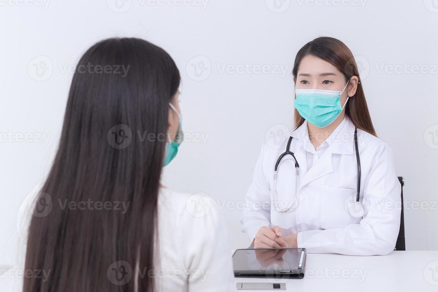 Asian woman patient consults her health with doctor, doctor give counsel with her while both wear medical face mask to protect infection disease in hospital. photo