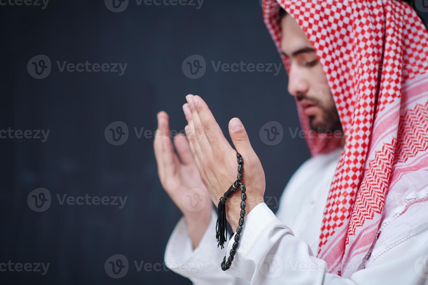 arabian man making traditional prayer to God, keeps hands in praying gesture in front of black chalkboard photo