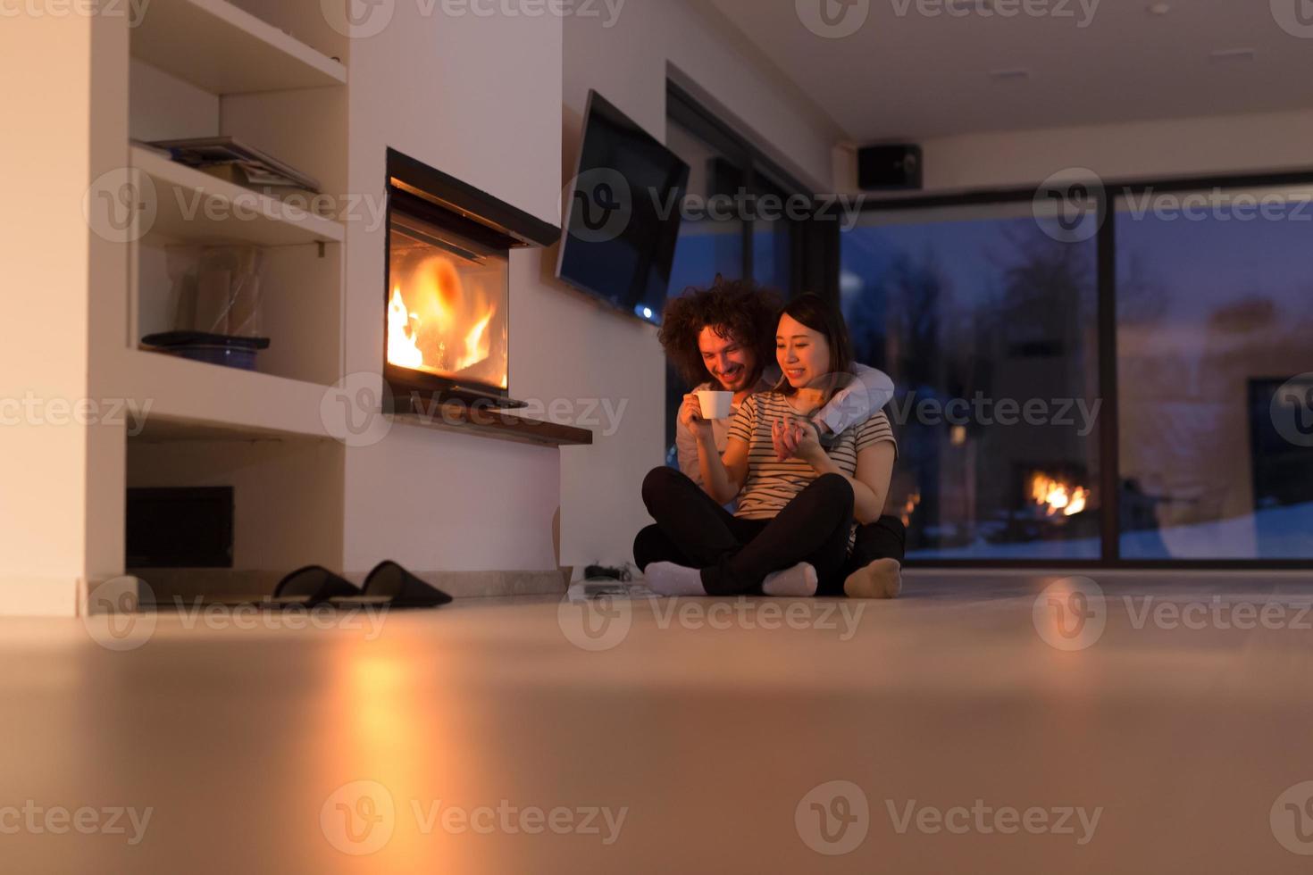 feliz pareja multiétnica sentada frente a la chimenea foto