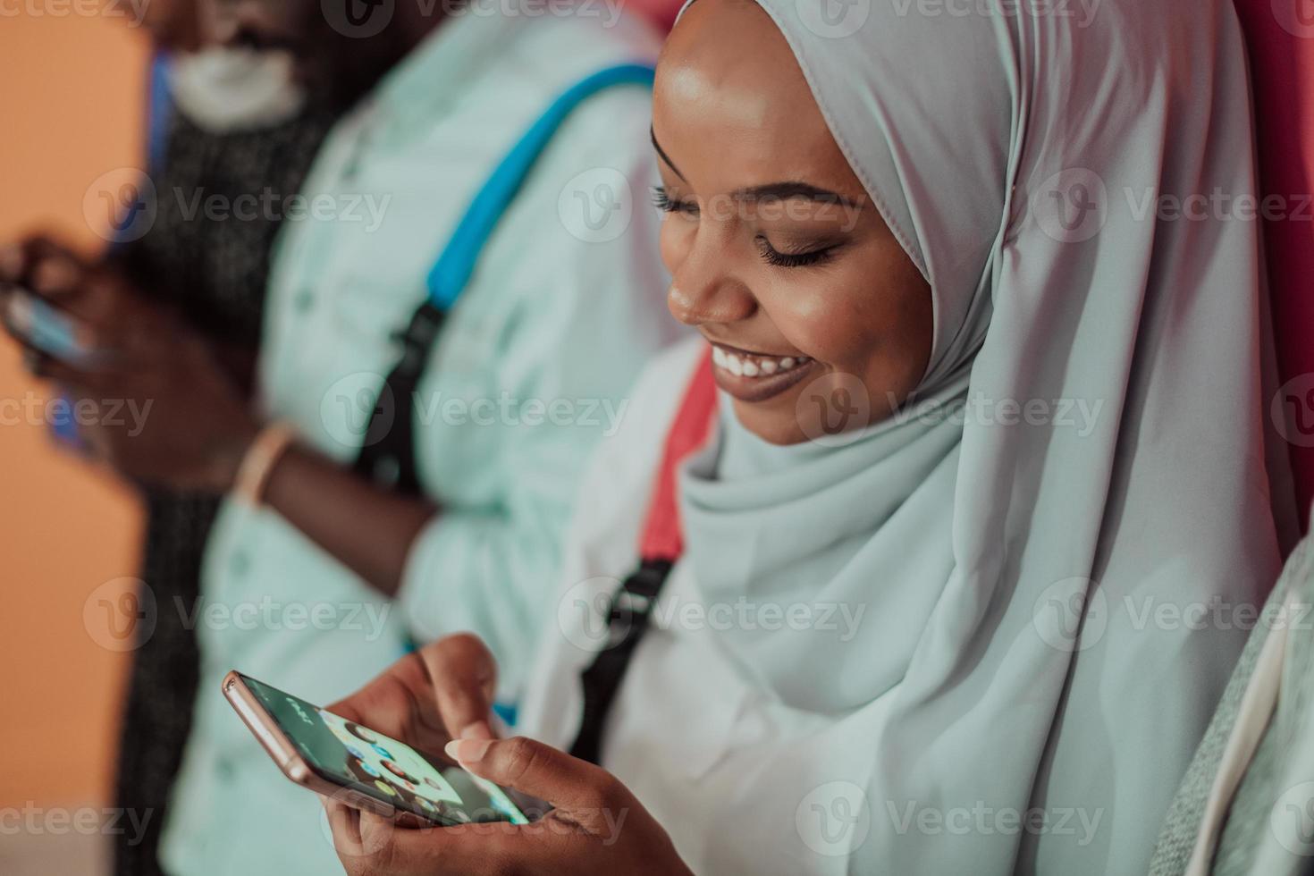 A group of African Muslim students use smartphones while standing in front of a yellow background photo