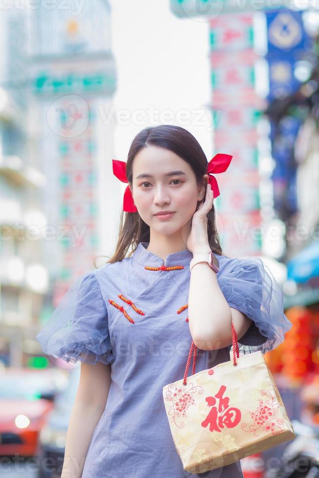 hermosa chica asiática vestida de chino está sonriendo sostiene la bolsa de tela que proyecta la palabra que significa feliz y caminando en la calle en la ciudad de china, tailandia. foto