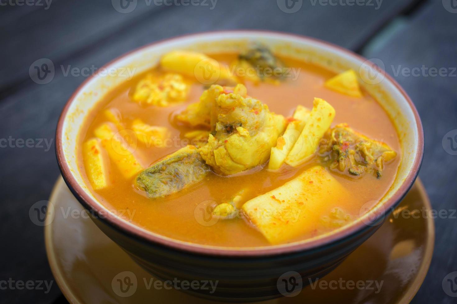 Spicy sour yellow curry with  coconut shoots and sea fish is one of Southern of Thai food on wood table as a background. photo