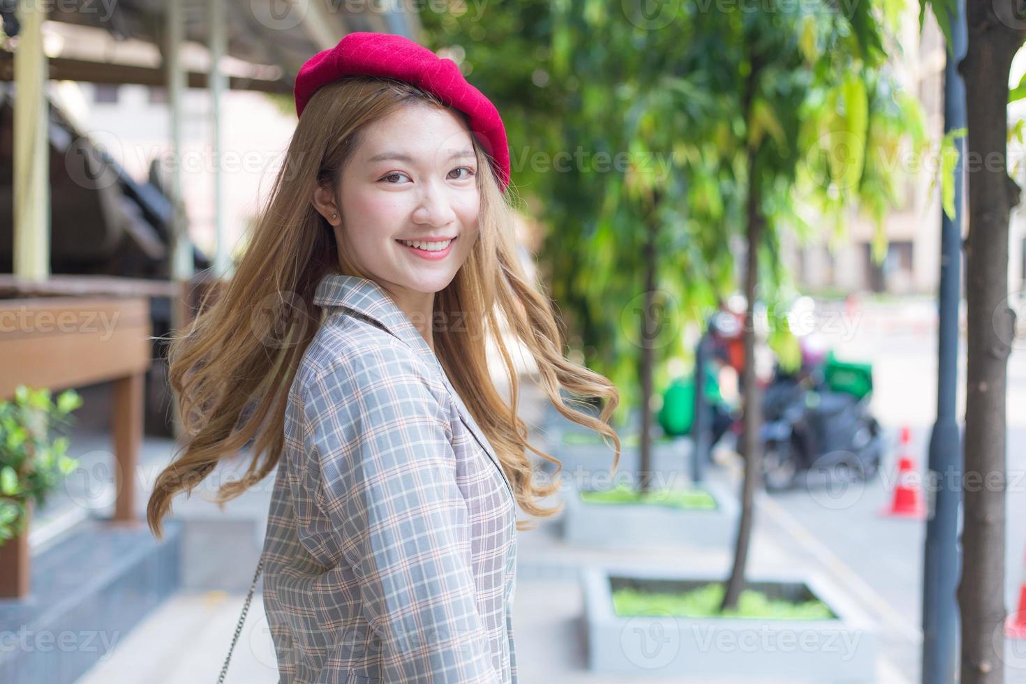 hermosa mujer asiática con cabello bronce lleva gorra roja y se vuelve hacia el fondo de la calle. foto