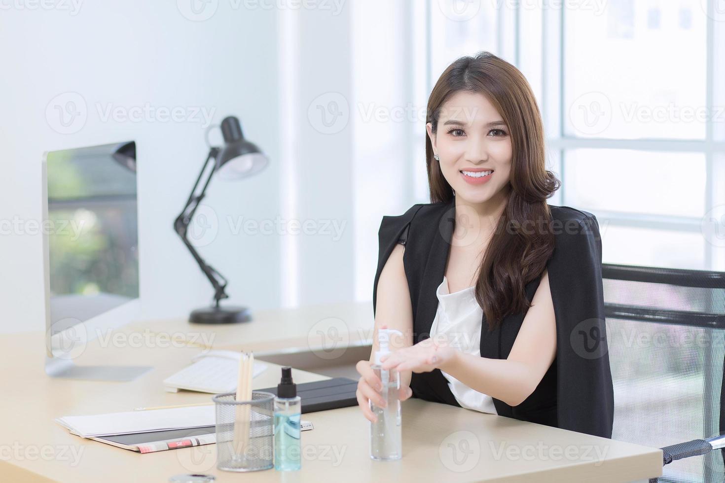 una bella oficinista está sentada y presionando un gel de alcohol para lavarse las manos en el lugar de trabajo. foto