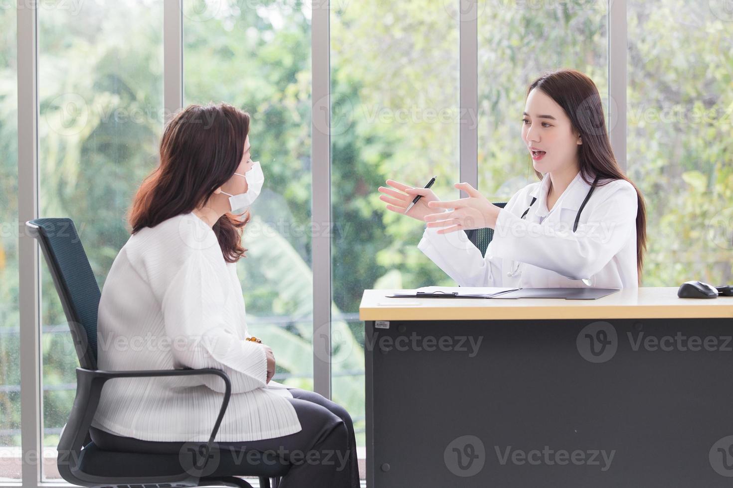 Asian doctor woman who wears medical coat talks with woman patient to suggest treatment guideline and healthcare concept in office of hospital. photo