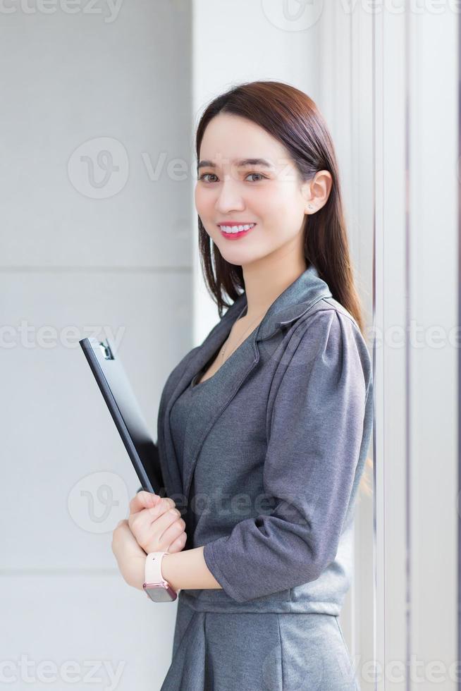 Asian business woman stands and holds notebook in her hands in workplace. photo