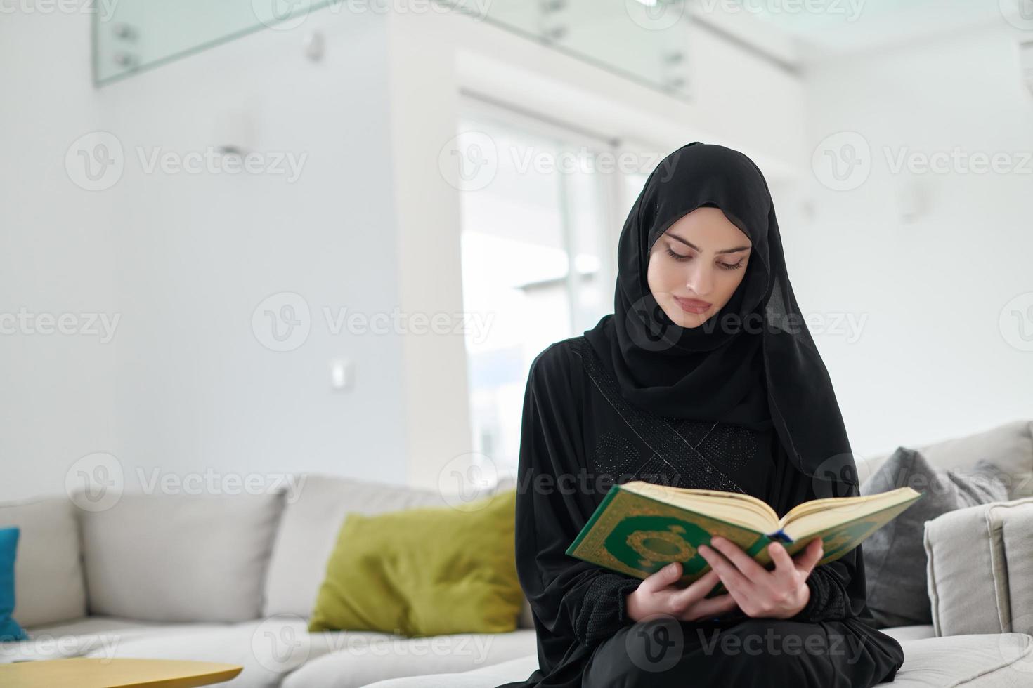 Portrait of young muslim woman reading Quran in modern home photo