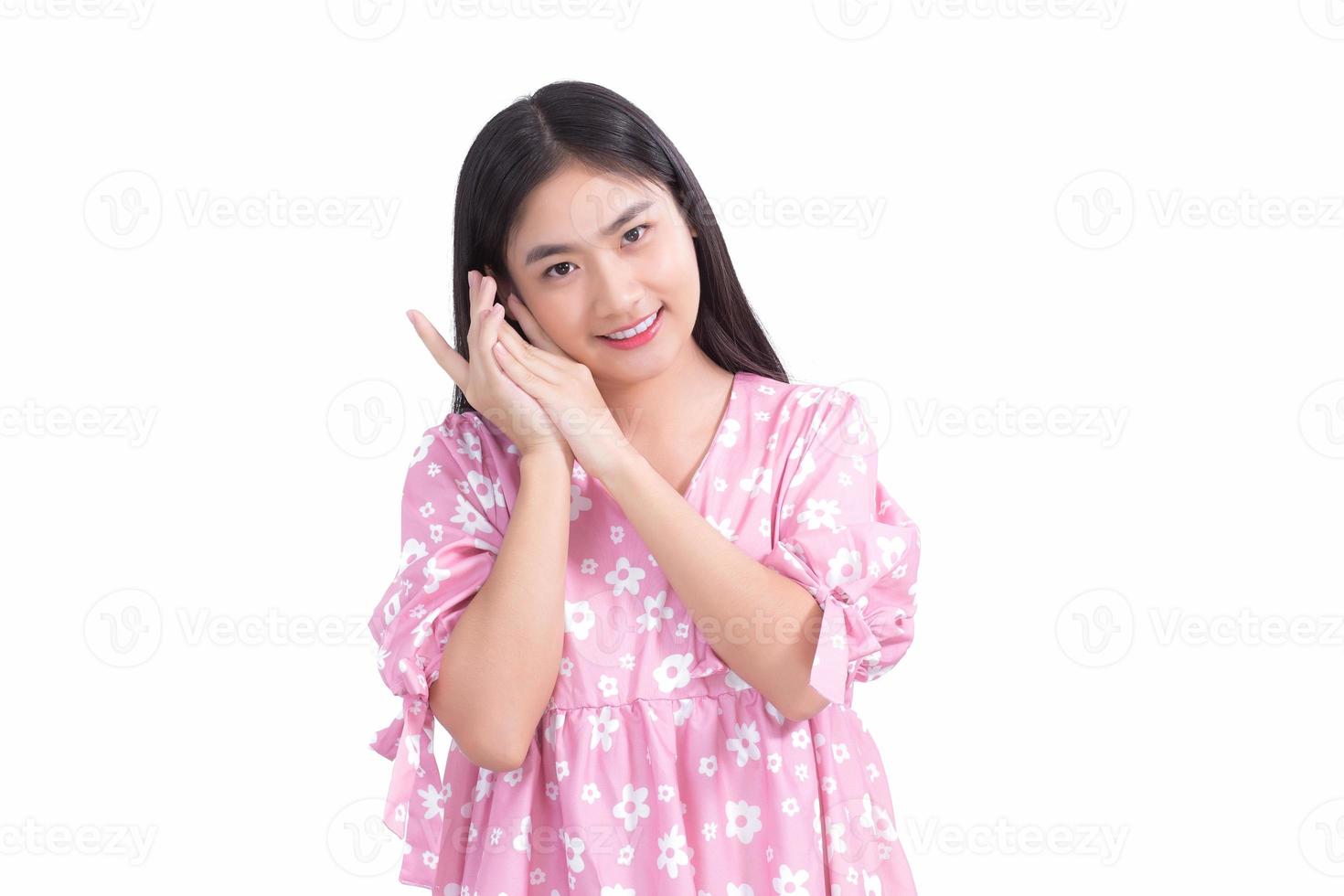 hermosa chica asiática con vestido rosa y pelo largo negro. sus manos tocan la sonrisa de la mejilla, muestran una piel hermosa sobre fondo blanco. foto