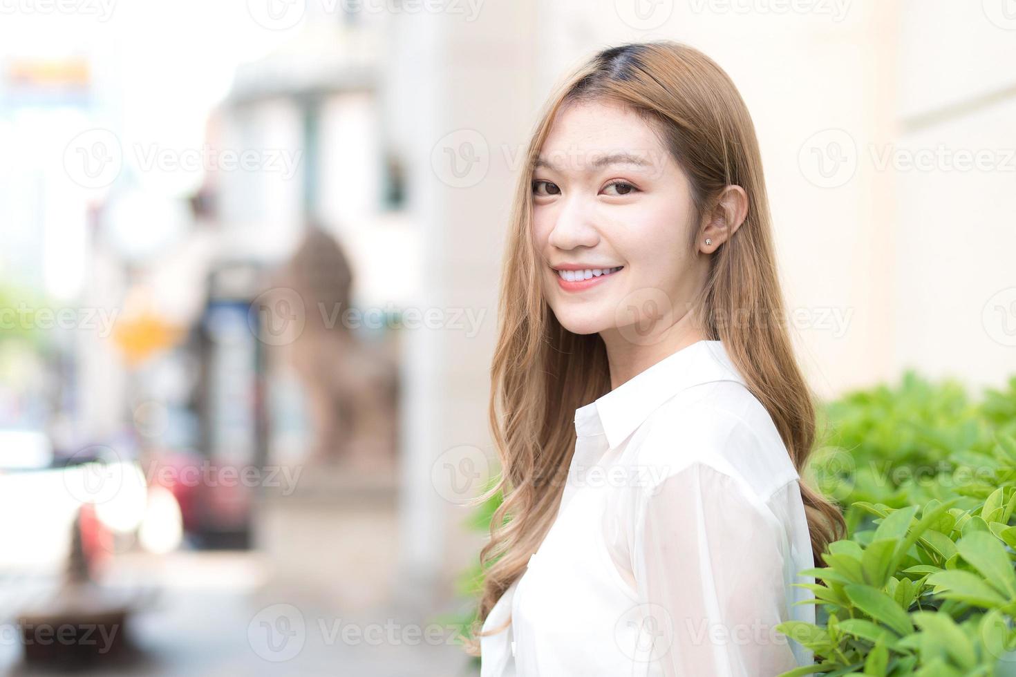 Asian beautiful girl with bronze hair  in white shirt while sits happy smilie on the edge of a city street. photo