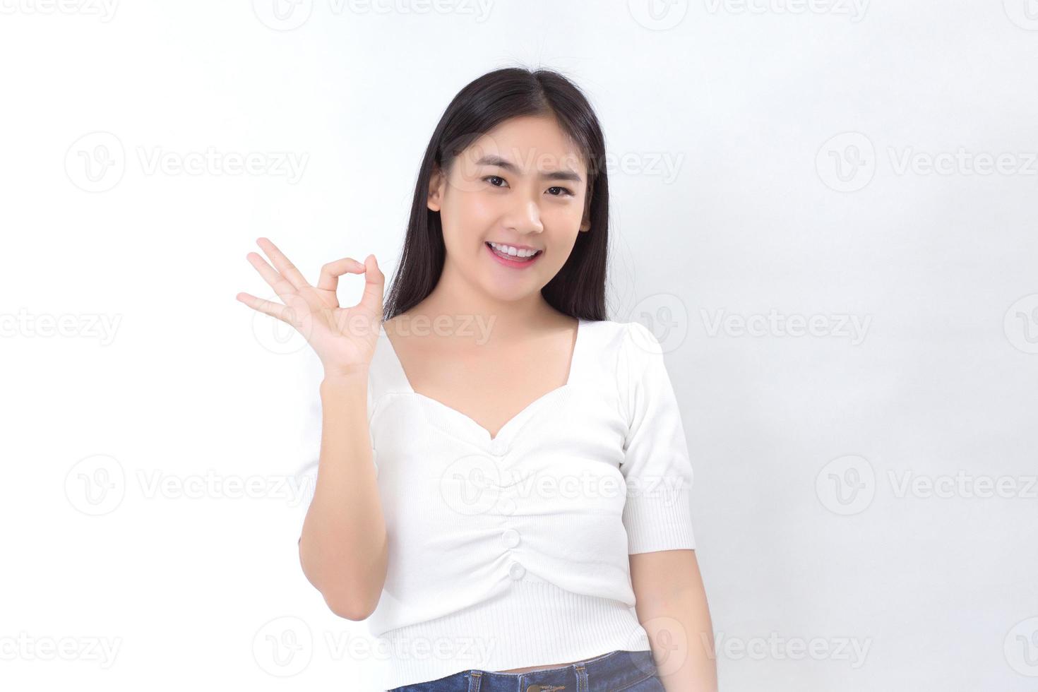 Asian beautiful woman with black long hair in white shirt shows hand ok sign on white background. photo