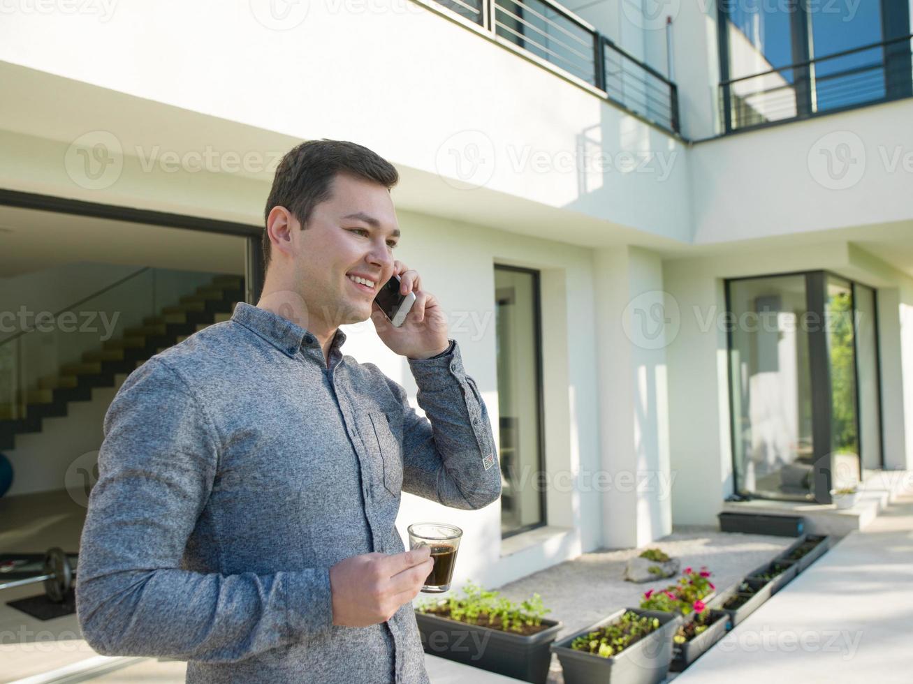 man using mobile phone in front of his luxury home villa photo