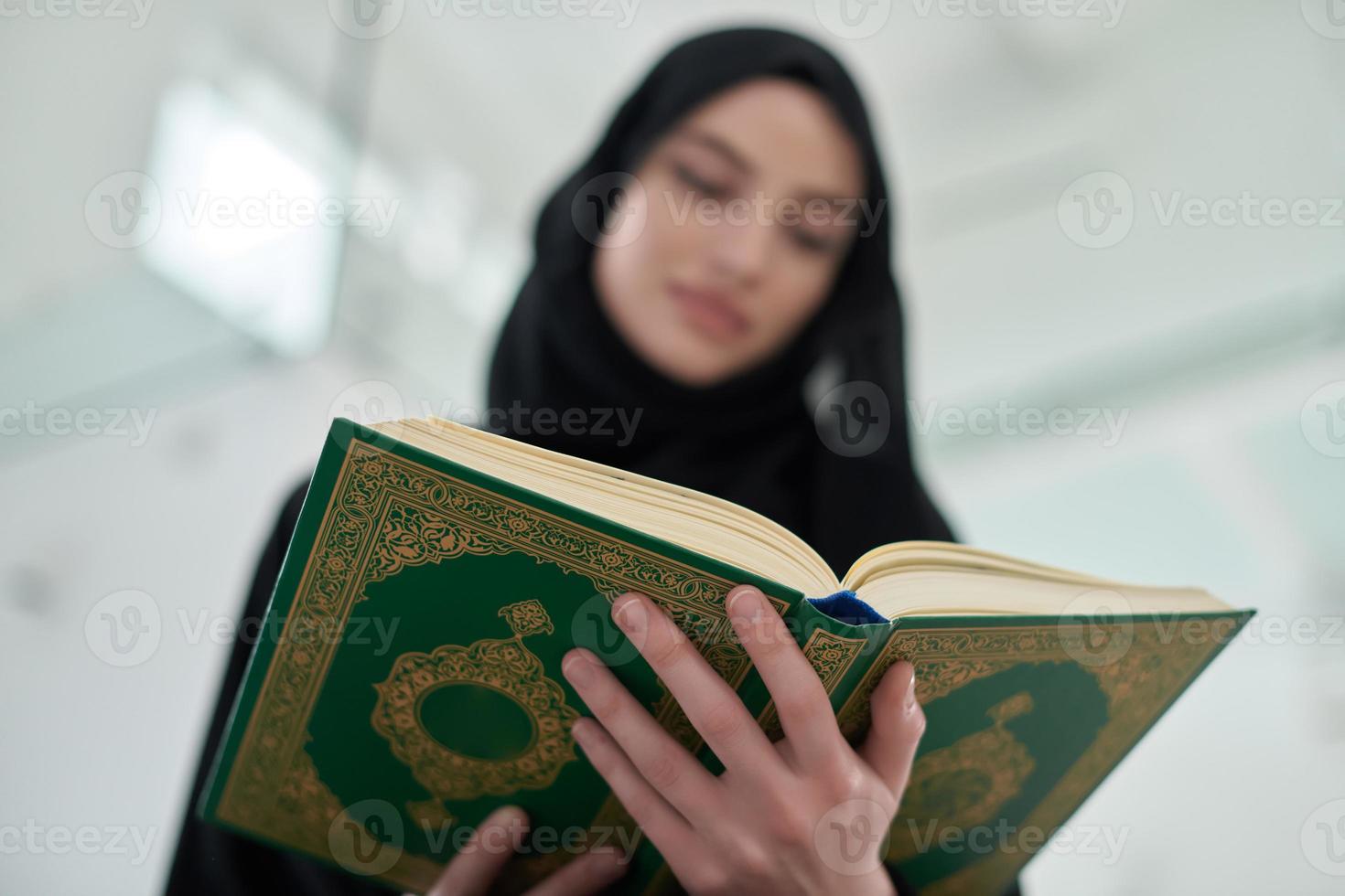 Portrait of young muslim woman reading Quran in modern home photo