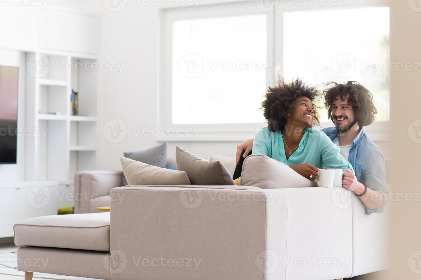 multiethnic couple sitting on sofa at home drinking coffe photo