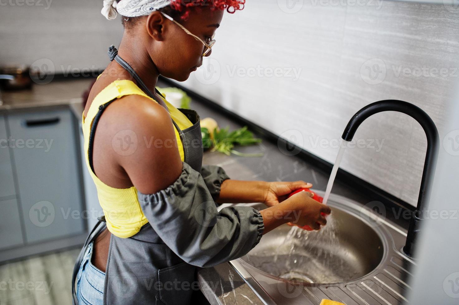 mujer afroamericana preparando comida saludable en la cocina de casa. ella lava los productos en el lavabo. foto