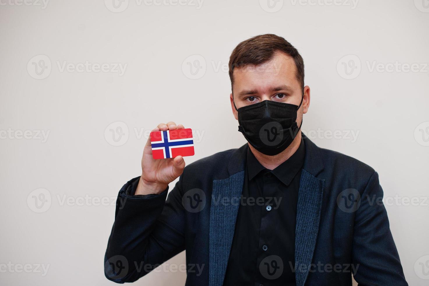 European man wear black formal and protect face mask, hold Norway flag card isolated on white background. Europe coronavirus Covid country concept. photo