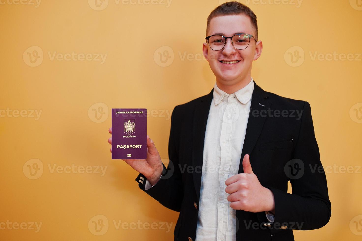 joven apuesto que tiene un pasaporte rumano de fondo amarillo, feliz y muestra el pulgar hacia arriba. viajar al concepto de país de europa. foto