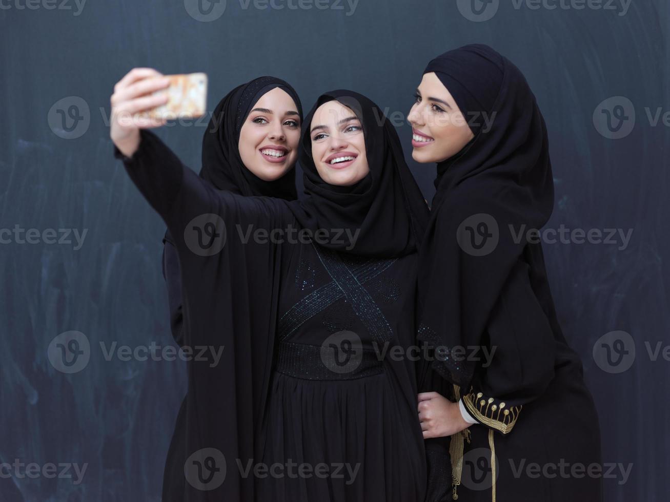 muslim women taking selfie picture in front of black chalkboard photo