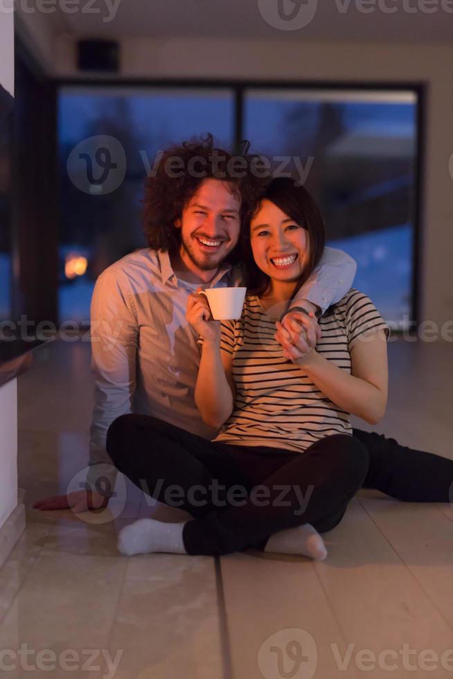 happy multiethnic couple sitting in front of fireplace photo