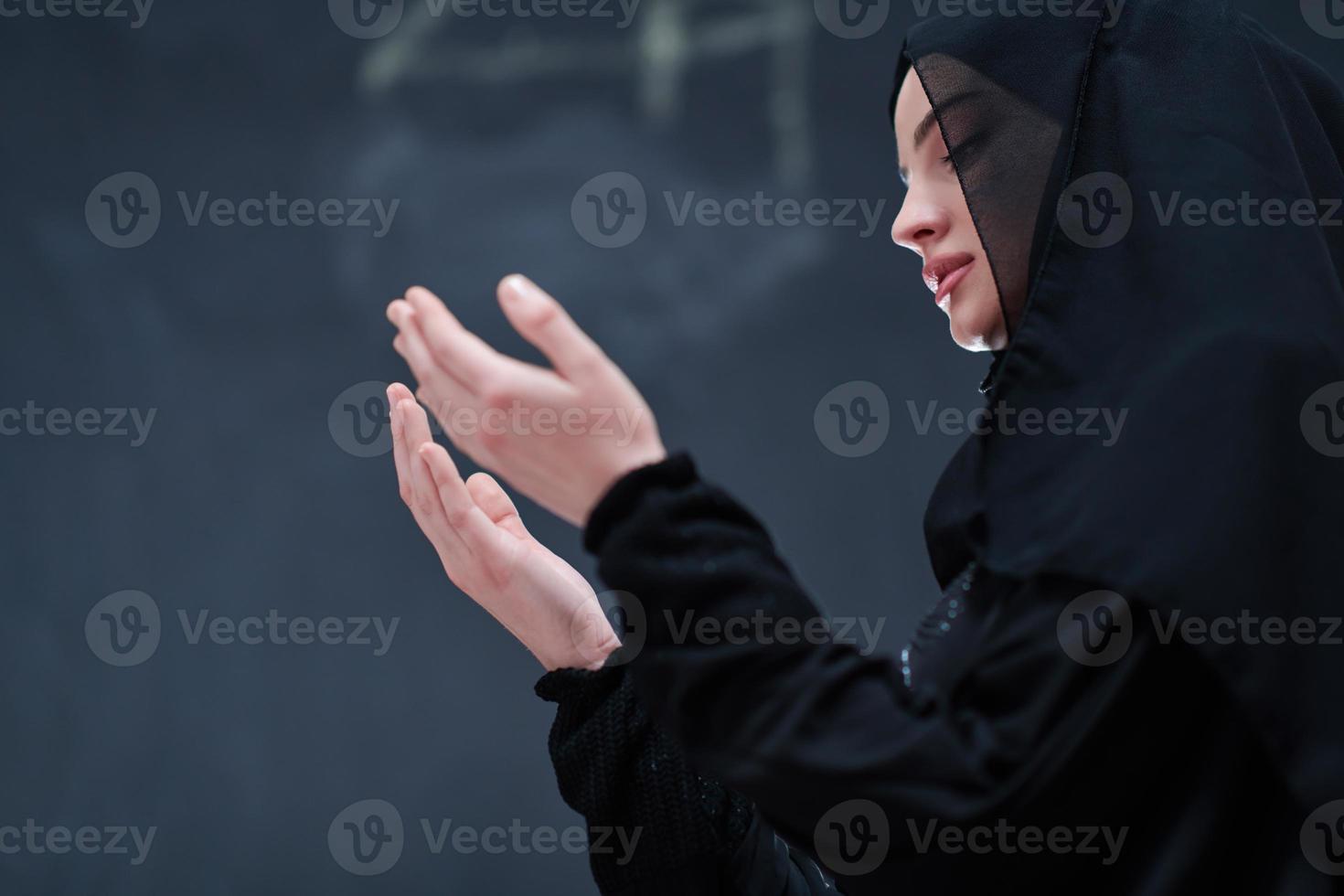 muslim woman making traditional prayer to God in front of black chalkboard photo