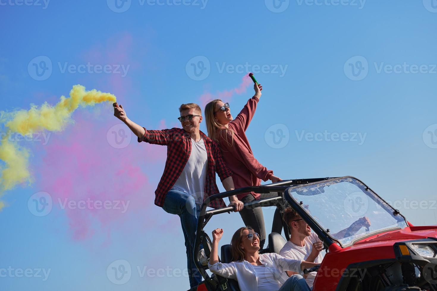 gente emocionada divirtiéndose disfrutando de un hermoso día soleado sosteniendo antorchas coloridas mientras conduce un coche de buggy fuera de la carretera foto