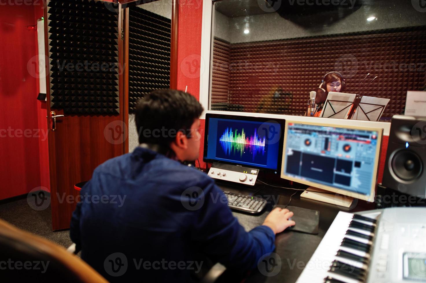 Young asian singer with microphone recording song in record music studio with sound producer. photo