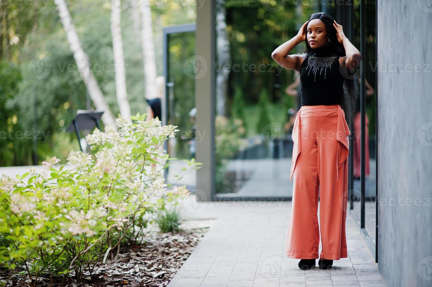 Fashionable african american woman in peach pants and black blouse pose outdoor. photo