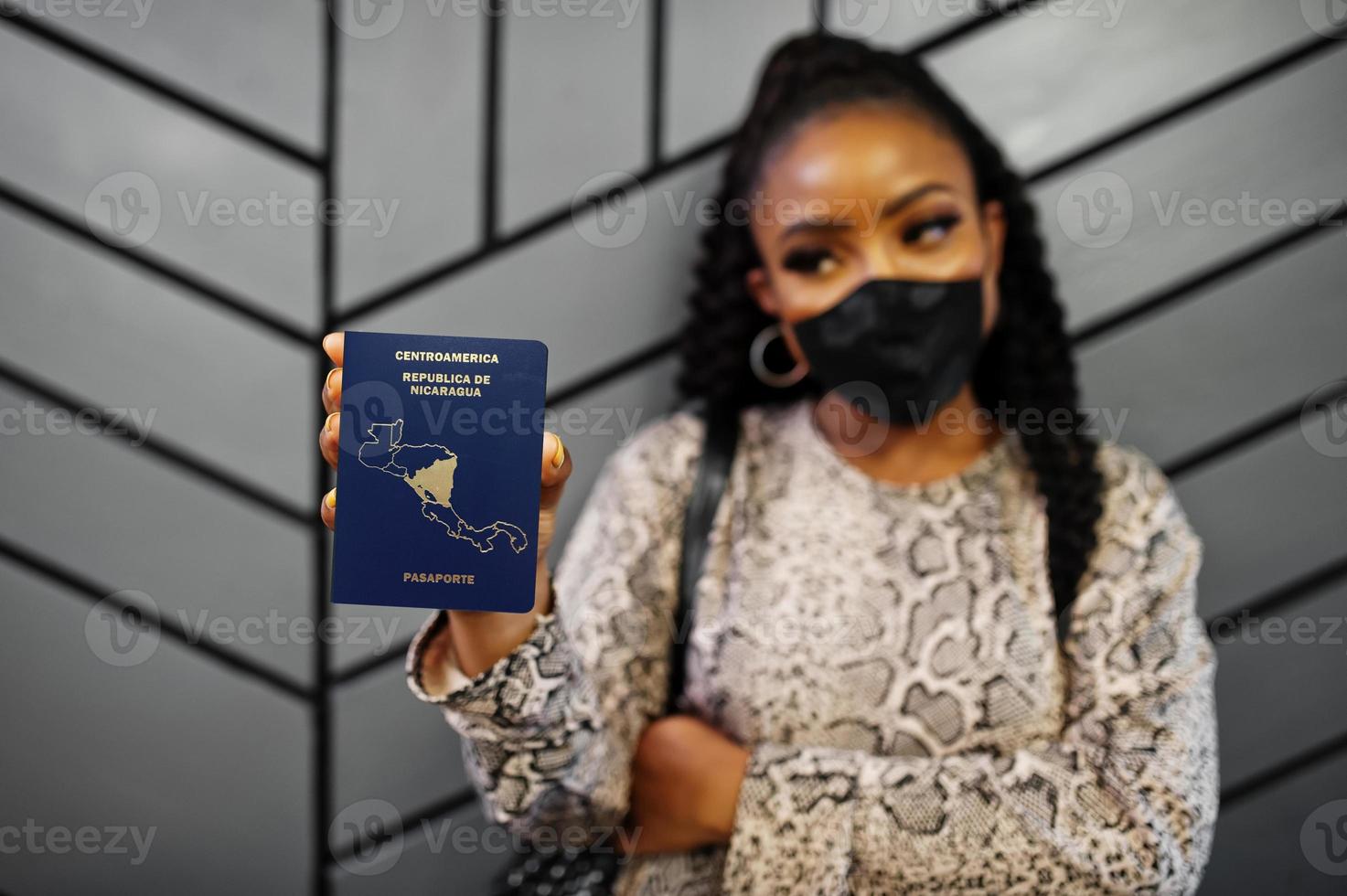 mujer afroamericana con mascarilla negra muestra el pasaporte de nicaragua en la mano. coronavirus en el país de América, cierre de fronteras y cuarentena, concepto de brote de virus. foto