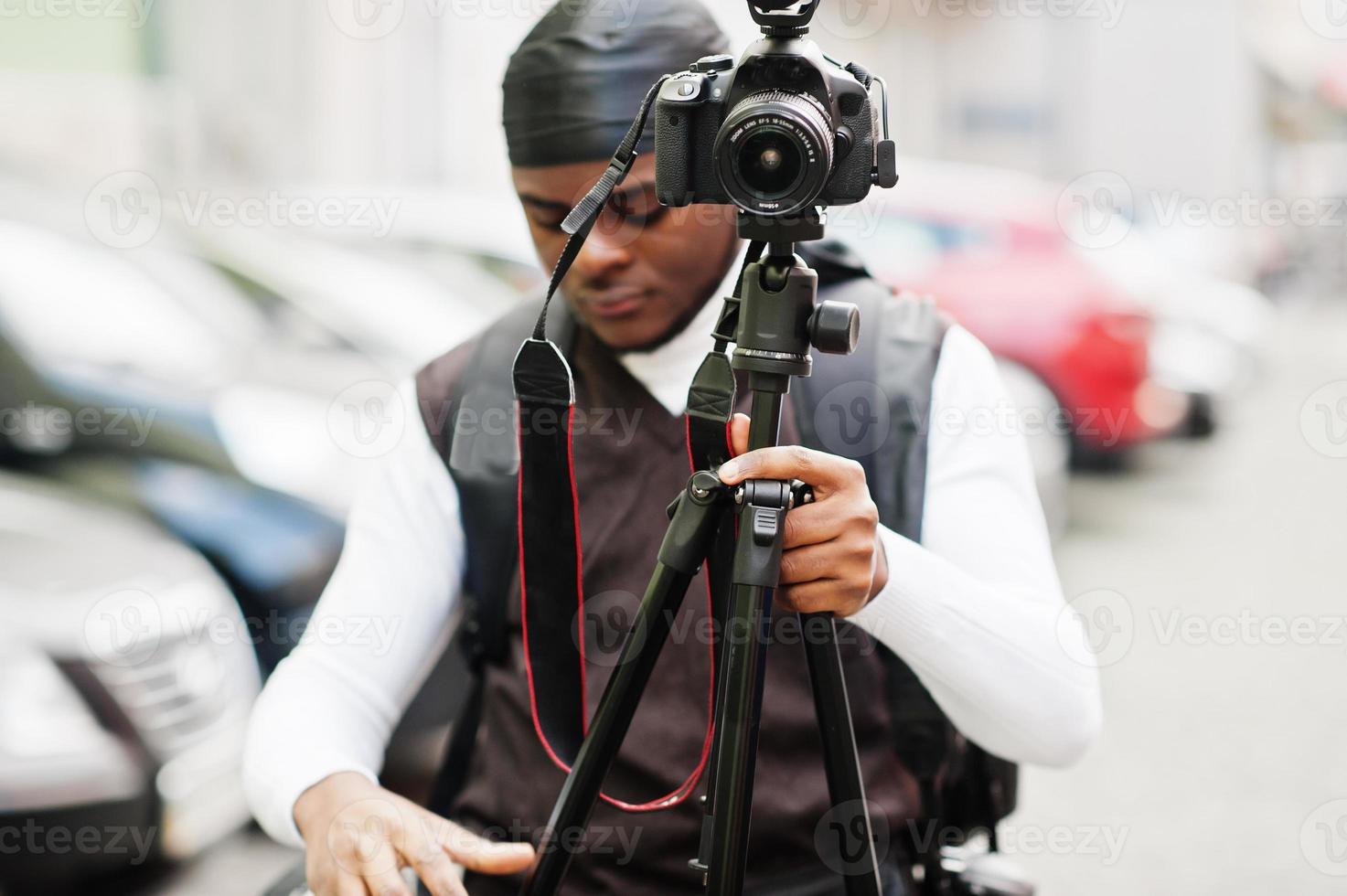 Young professional african american videographer holding professional camera with tripod pro equipment. Afro cameraman wearing black duraq making a videos. photo