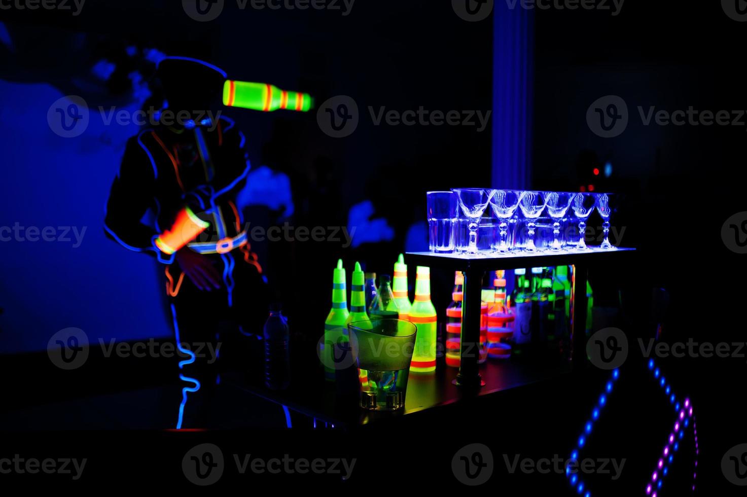 Professional barman and led light show. Silhouette of modern bartender shaking drink at night cocktail bar. photo