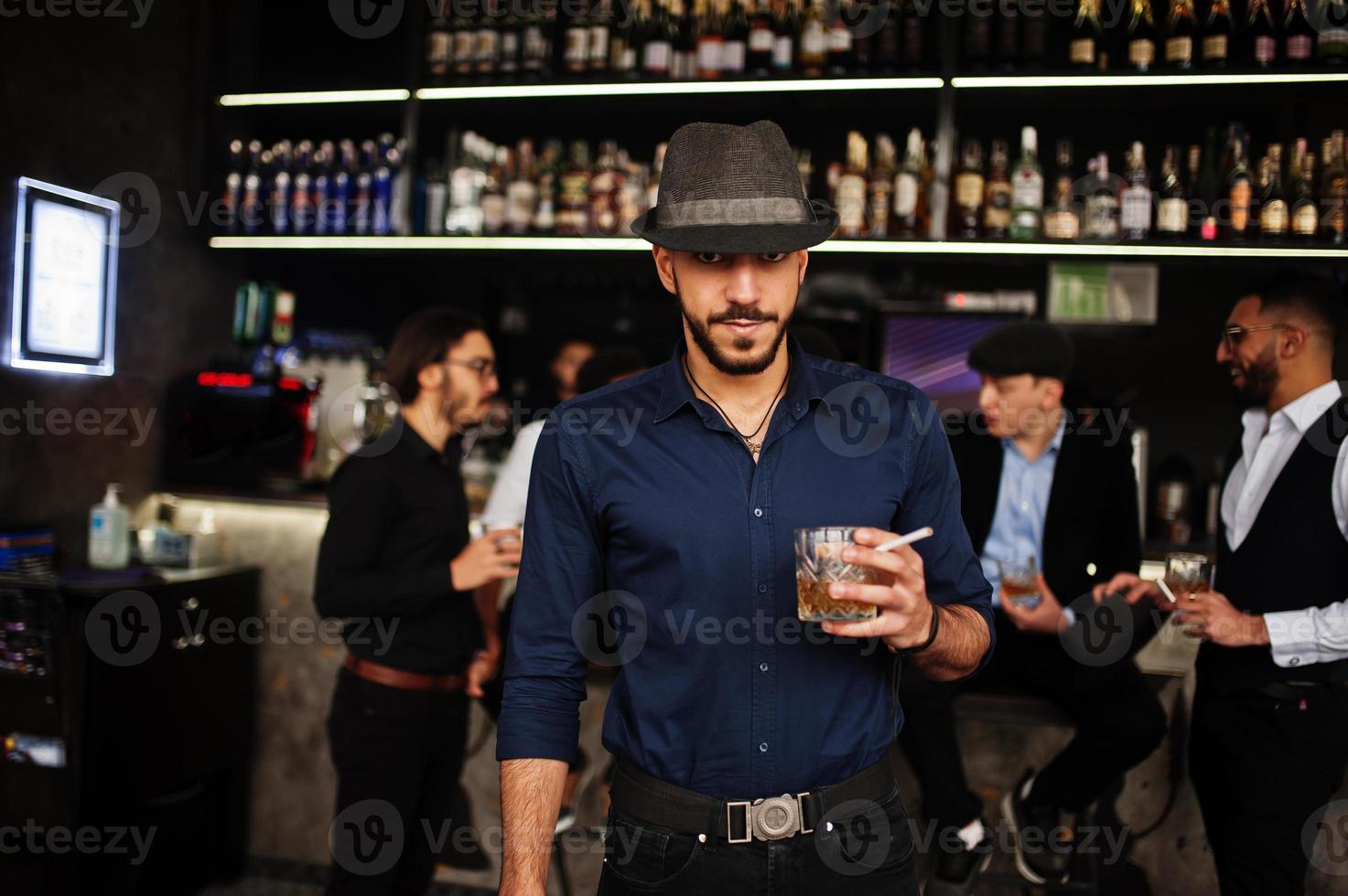 hombre árabe con estilo contra un grupo de gánsteres guapos retro bien vestidos pasan tiempo en el club, bebiendo en el mostrador del bar. despedida de soltero multiétnico de la mafia en el restaurante. foto