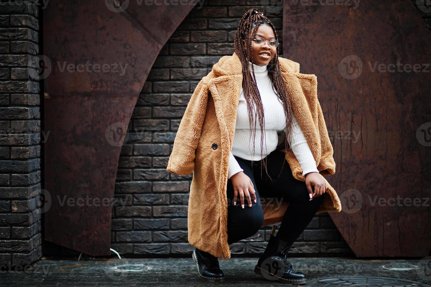 glamorosa mujer afroamericana en cálido abrigo de piel, anteojos posan en la calle. foto