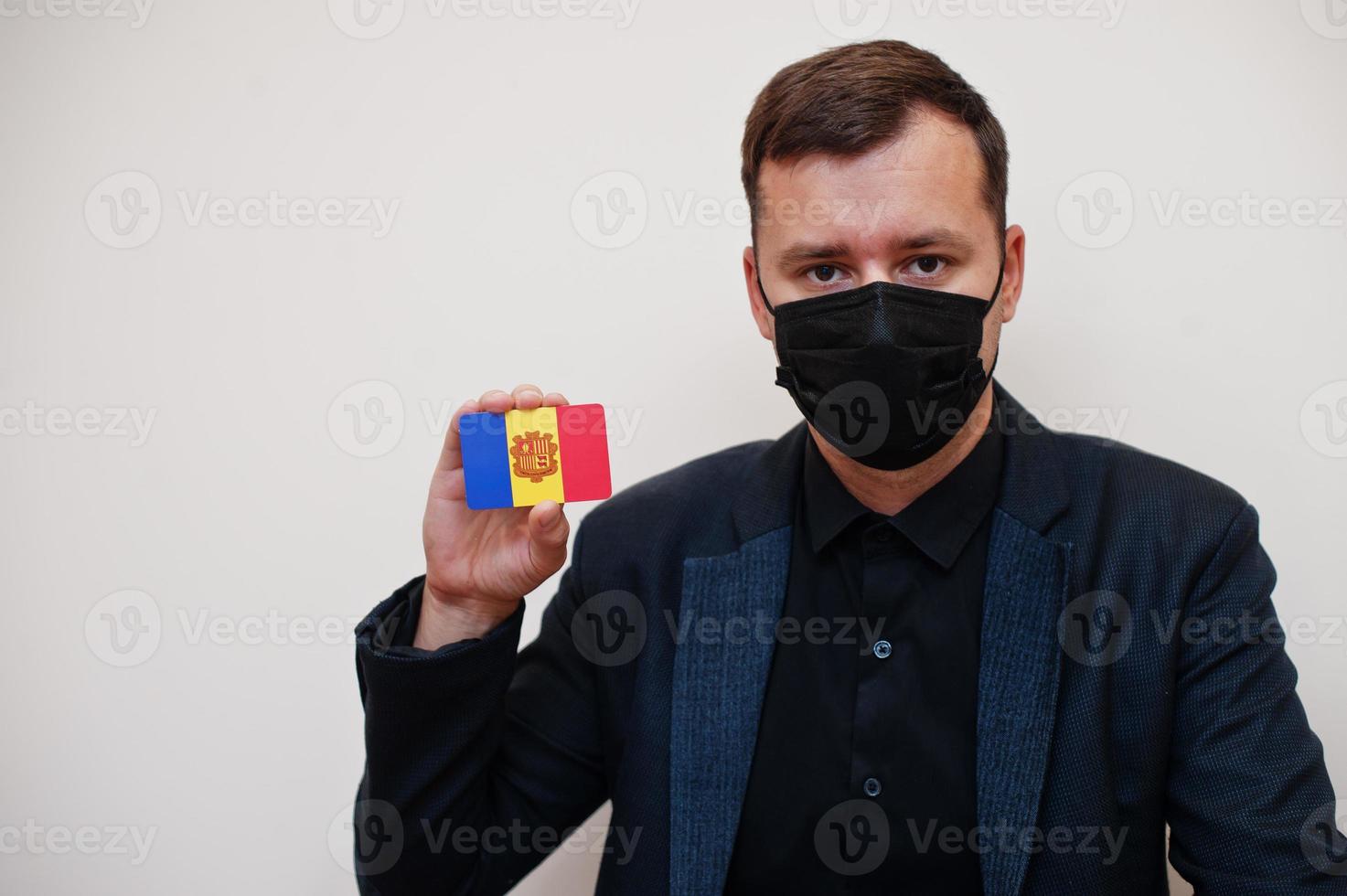 European man wear black formal and protect face mask, hold Andorra flag card isolated on white background. Europe coronavirus Covid country concept. photo