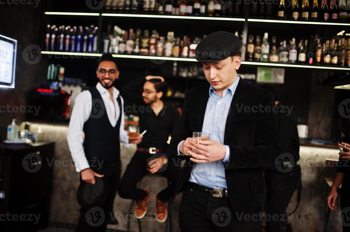 Stylish arab man against group of handsome retro well-dressed guys gangsters spend time at club, drinking on bar counter. Multiethnic male bachelor mafia party in restaurant. photo