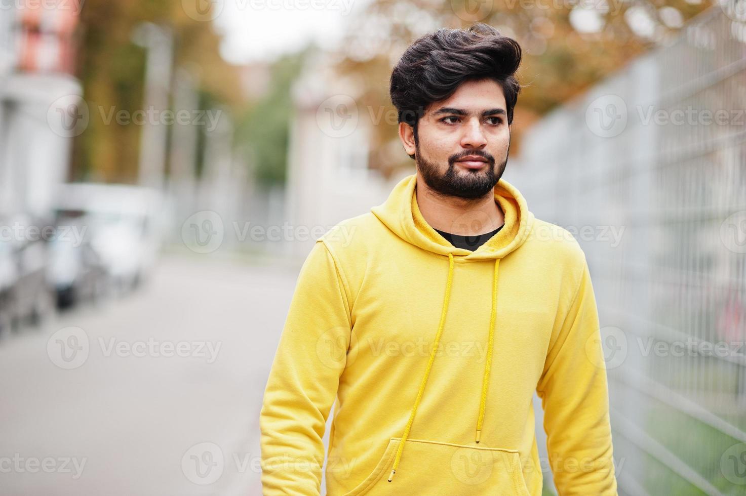 hombre indio joven hipster urbano en una sudadera amarilla de moda. Un chico genial del sur de Asia usa una sudadera con capucha caminando en Fall Street. foto