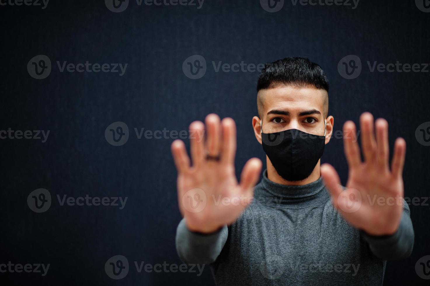 Middle eastern man in gray turtleneck and black face protect mask on isolated background show two hands, stop sign. photo