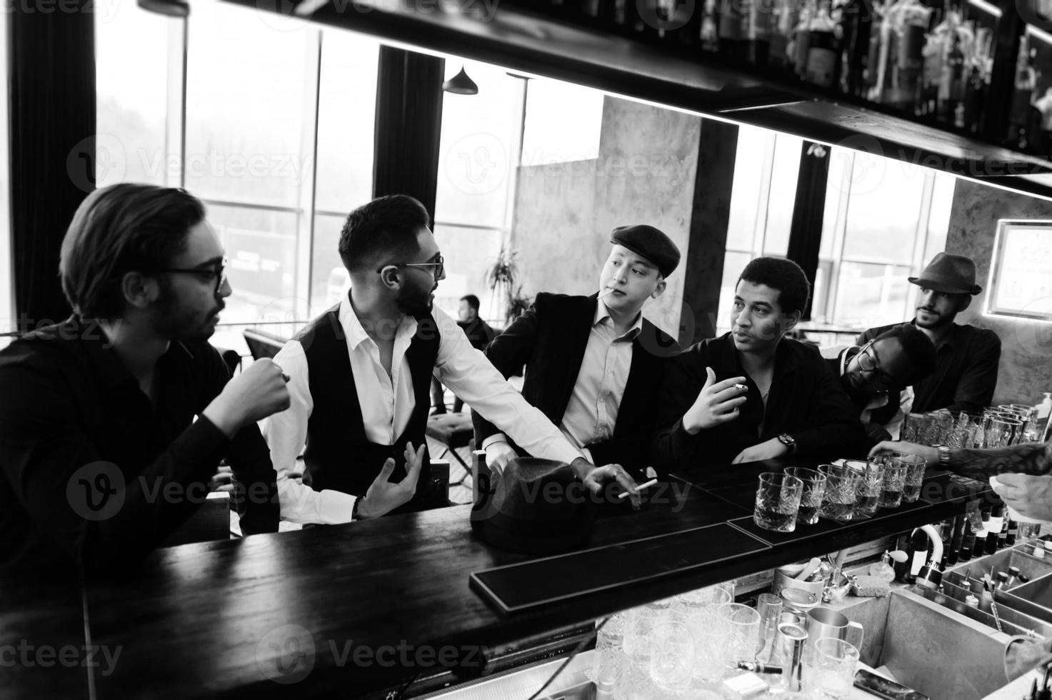 Group of handsome retro well-dressed man gangsters spend time at club. Drinking whiskey at bar counter. Multiethnic male bachelor mafia party in restaurant. photo