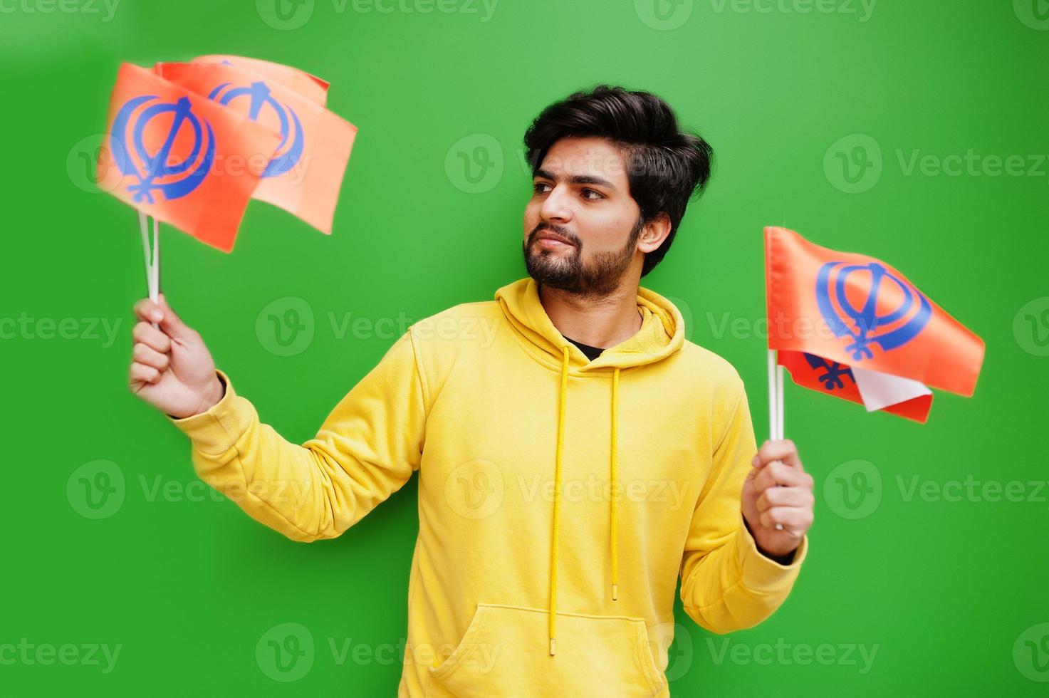Happy Guru Nanak Jayanti concept. Young indian man in yellow sweatshirt hold flags. Cool south asian guy wear hoodie celebrating India holiday. photo