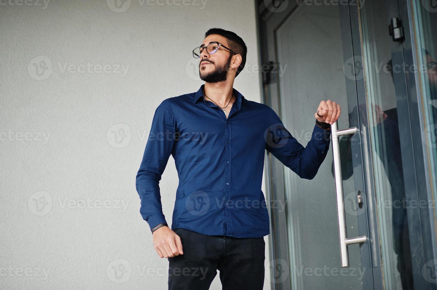 Middle eastern entrepreneur wear blue shirt, eyeglasses against office building. photo