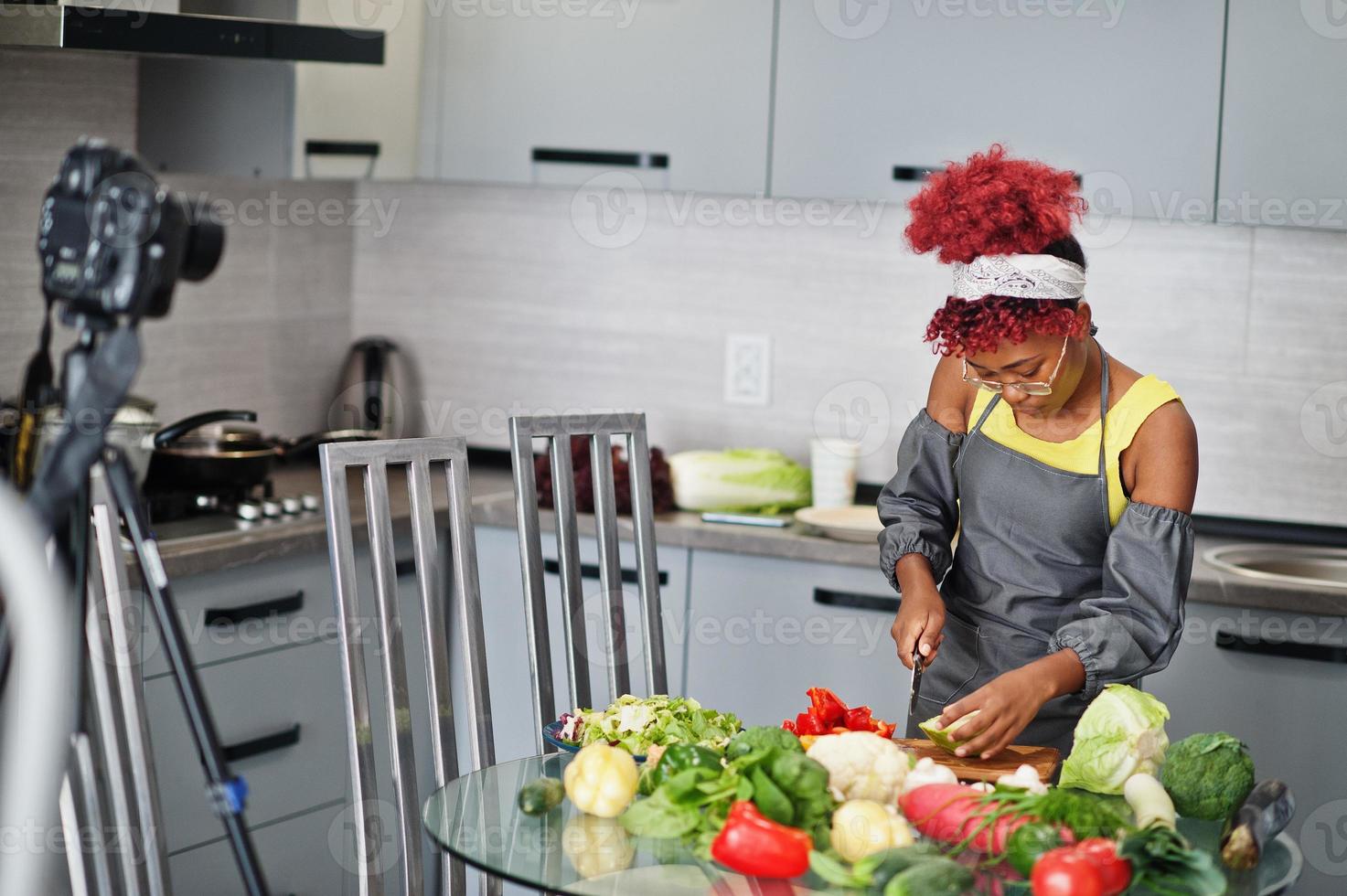 African american woman filming her blog broadcast about healthy food at home kitchen. She cuts the cabbage. photo