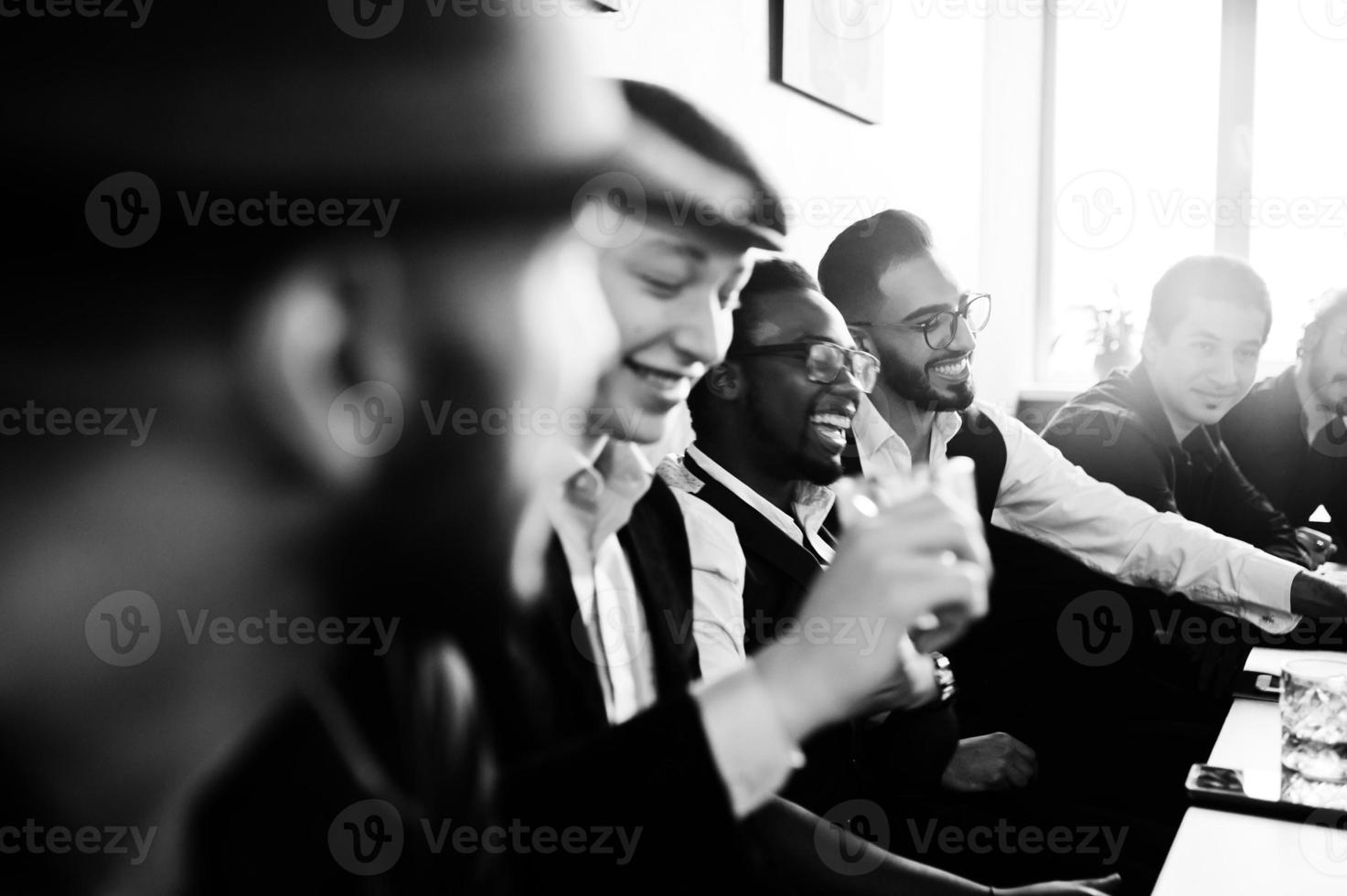 Group of handsome retro well-dressed man gangsters spend time at club, sitting and drinking whiskey. Multiethnic male bachelor mafia party in restaurant. photo