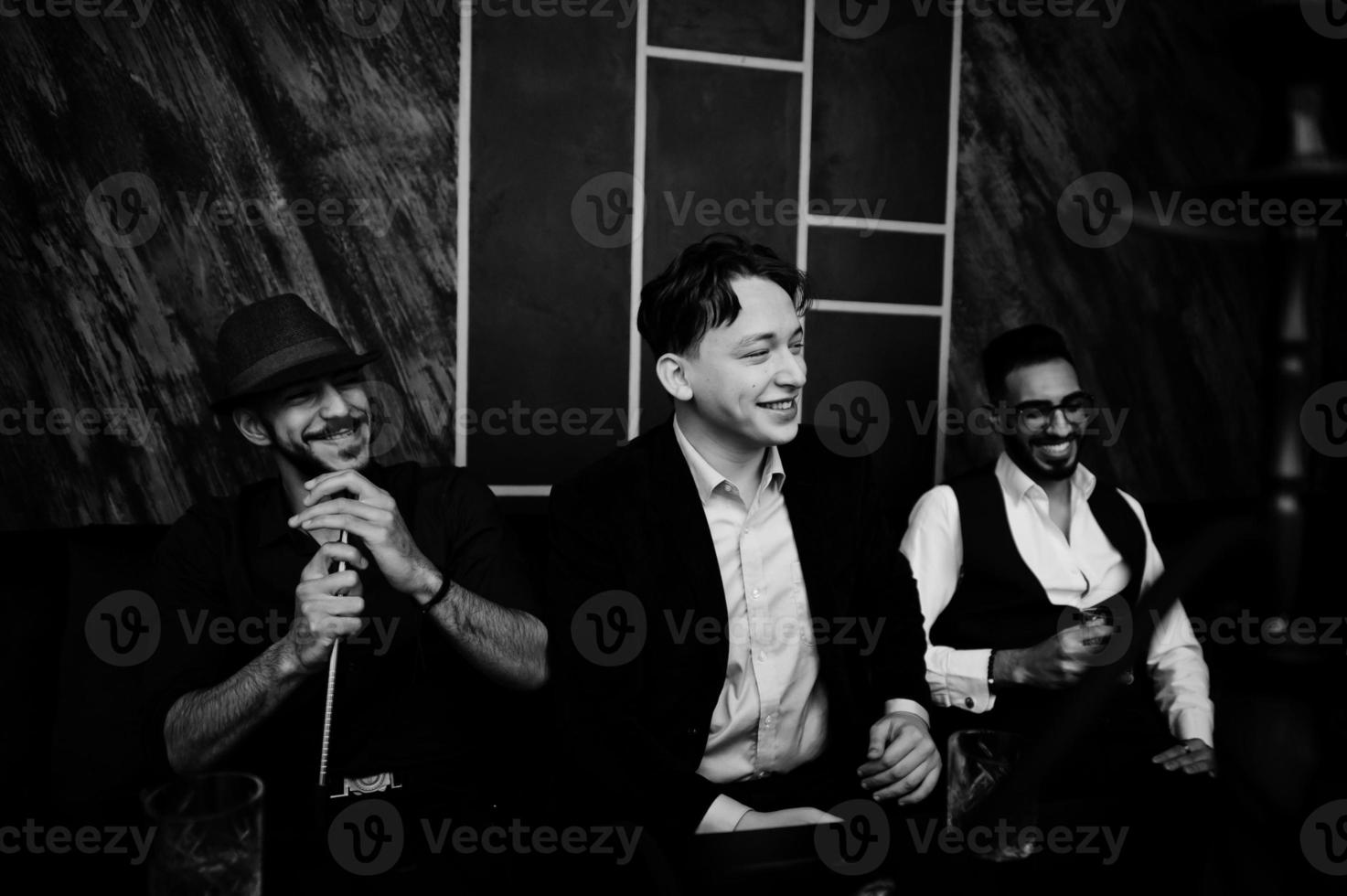 Group of handsome retro well-dressed man gangsters spend time at club, smoking hookah. Multiethnic male bachelor mafia party in restaurant. photo