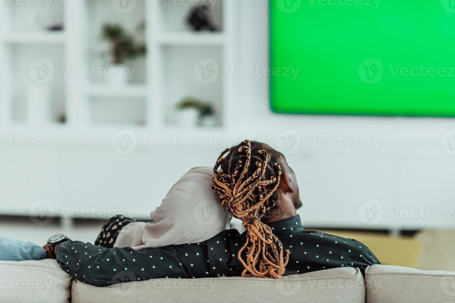African Couple Sitting On Sofa Watching TV Together Chroma Green Screen Woman Wearing Islamic Hijab Clothes photo