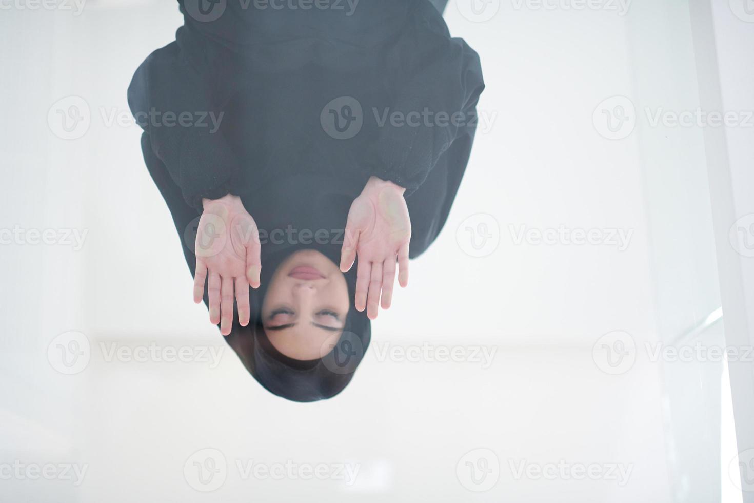 young arabian muslim woman praying on the glass floor at home photo